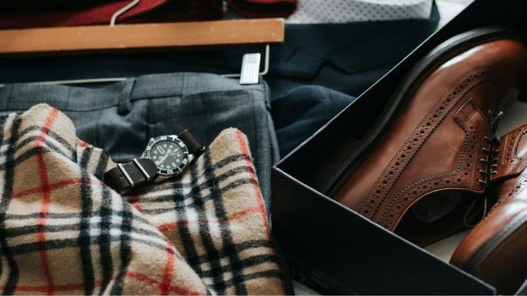 A pair of brown shoes, a stylish watch, and a pair of pants arranged neatly on a surface.