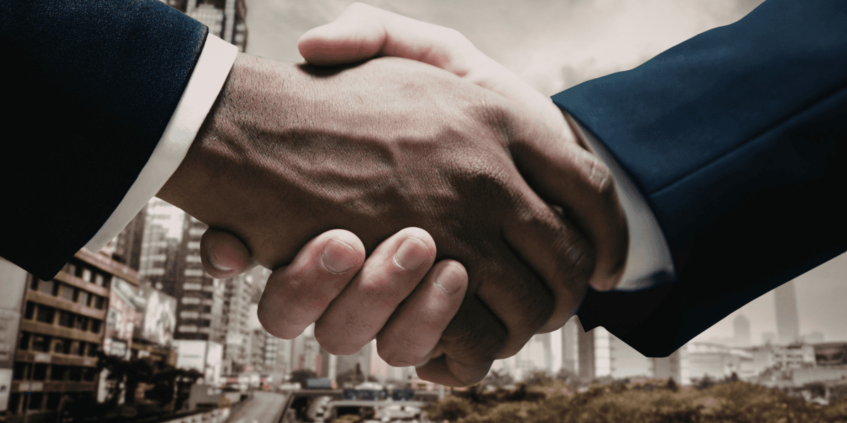 Two hands shake in a business setting with a cityscape in the background