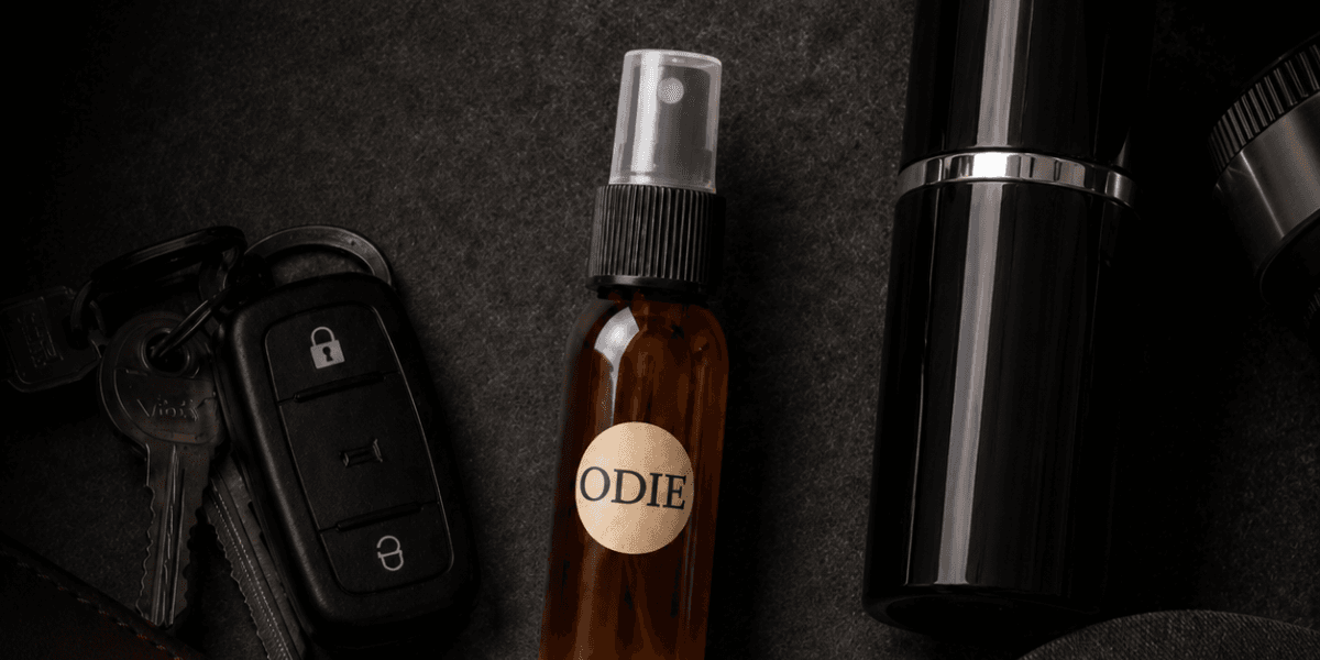 Flat lay of a brown spray bottle labeled "ODIE," car keys, and a black container