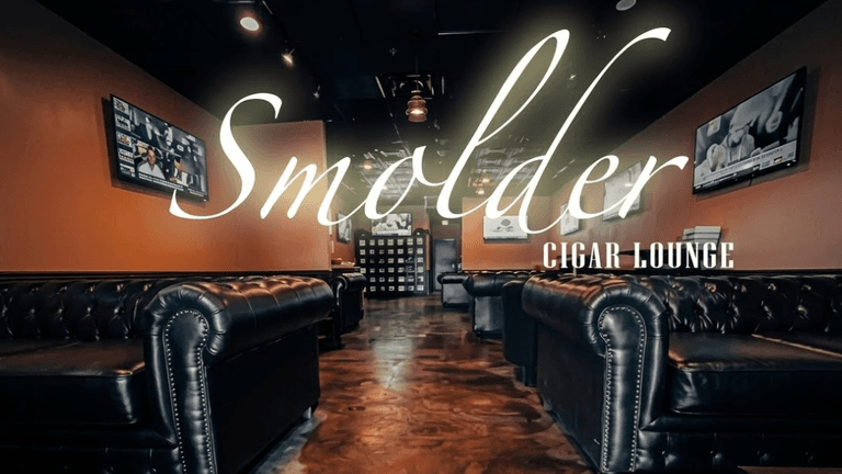 Interior of Smolder Cigar Lounge with leather sofas, TVs, warm lighting, and elegant signage.