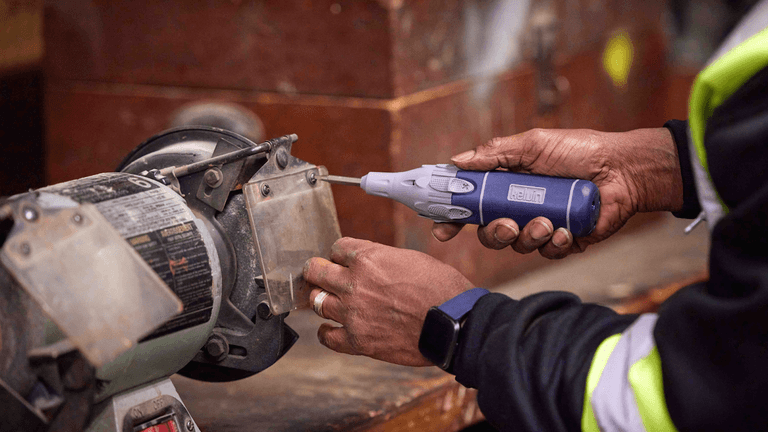 An African American technician uses a Kelvin Retractor Series screwdriver to secure a protective shield on a workbench grinder.