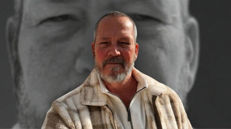 Portrait of a bearded man in front of a large grayscale face backdrop.