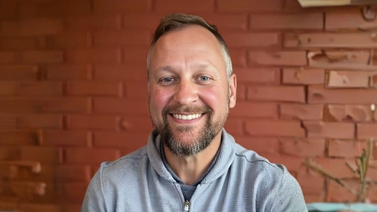 Mike Snellenberger, founder of The Fractional CMO Team, smiles in front of a textured brick wall, embodying strategic leadership.