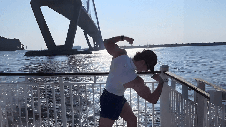 Brandon Stalter flexing by the water under a bridge, embodying strength, resilience, and transformation in his fitness journey.