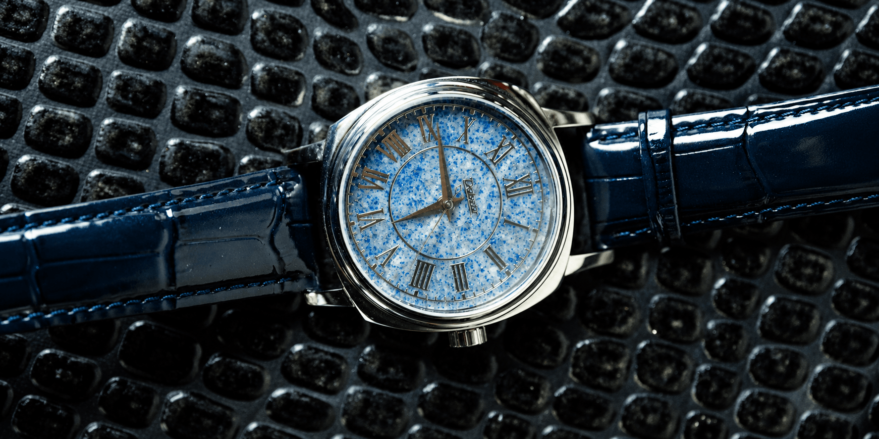 Elegant watch with a blue speckled dial and navy crocodile leather strap on textured surface