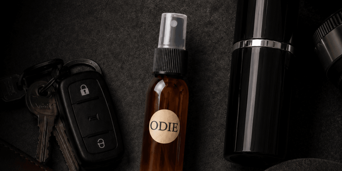Flat lay of a brown spray bottle labeled "ODIE," car keys, and a black container