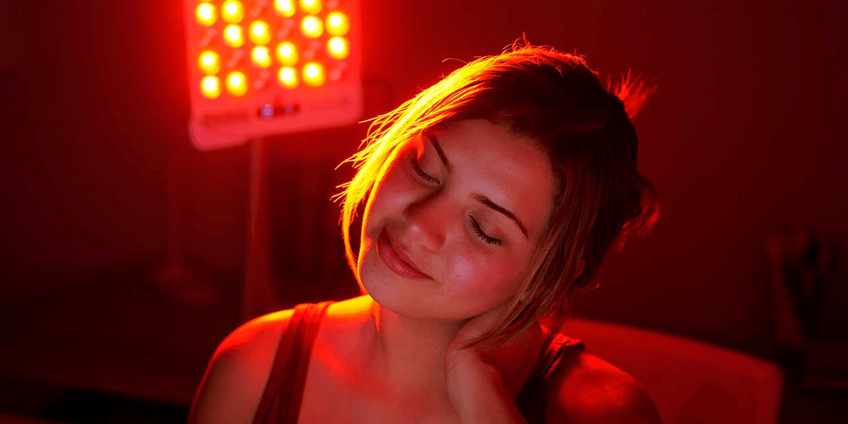 Woman enjoying red light therapy, relaxing with a gentle smile in dim lighting