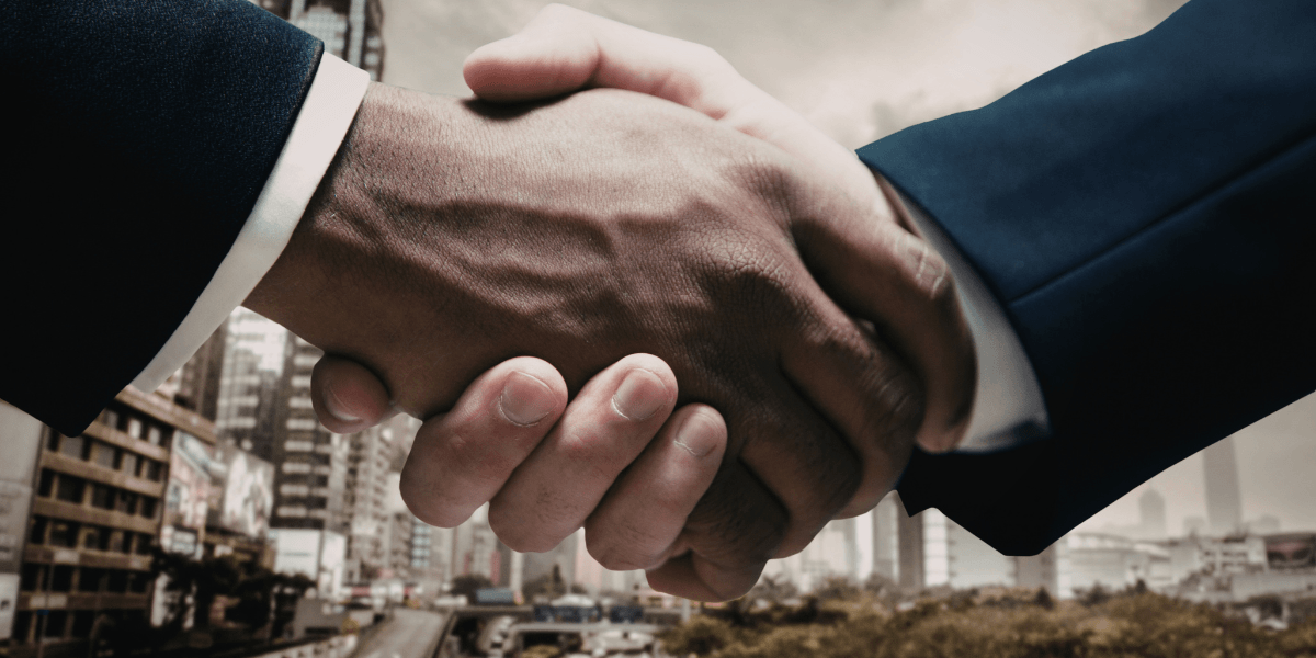 Two hands shake in a business setting with a cityscape in the background