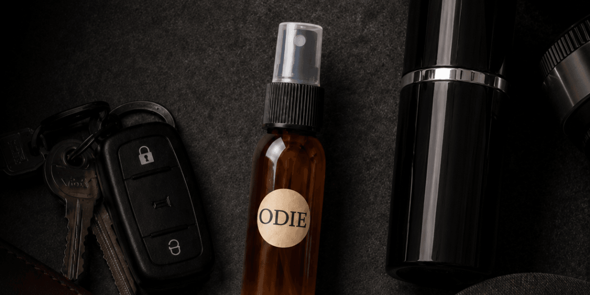 Flat lay of a brown spray bottle labeled "ODIE," car keys, and a black container