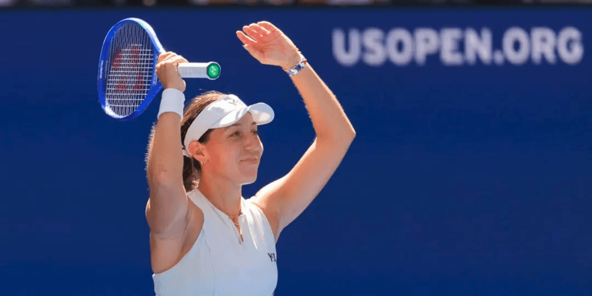 Smiling tennis player raises her arms in celebration on the court.