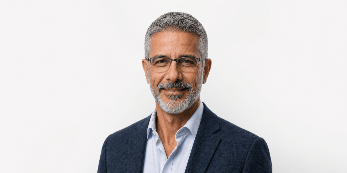 Smiling man with gray hair and glasses wearing a blue blazer over a white shirt