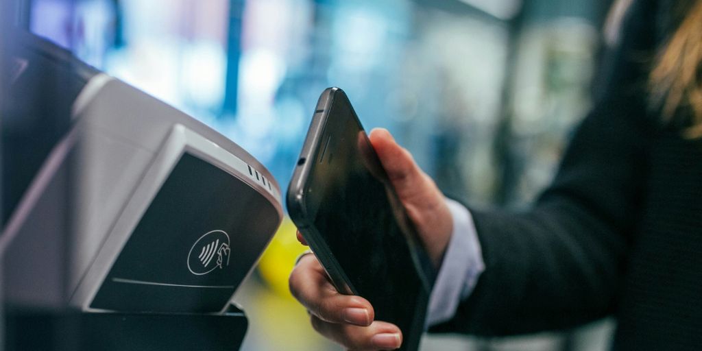 A person operates a machine with one hand while holding a phone in the other hand.