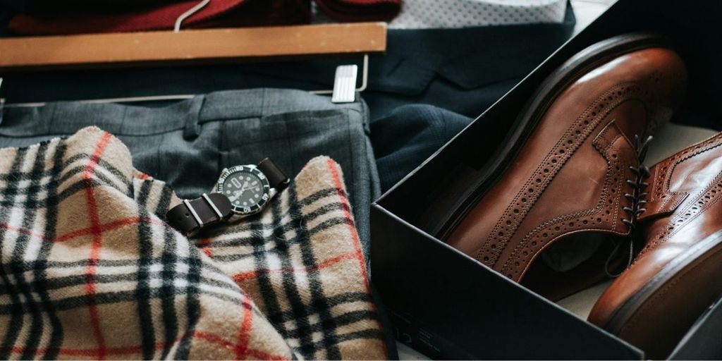A pair of brown shoes, a stylish watch, and a pair of pants arranged neatly on a surface.