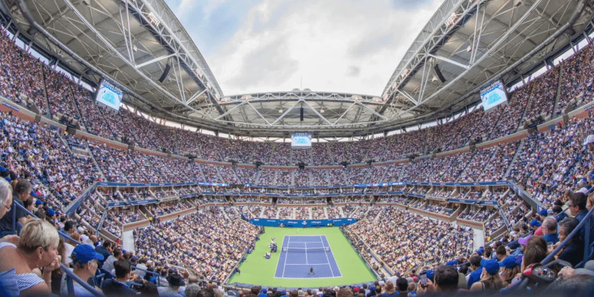 Packed stadium during a tennis match with a large audience and bright sky