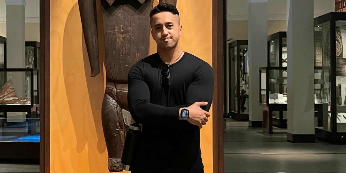 Man in a museum posing beside a large wooden artifact wearing a black shirt