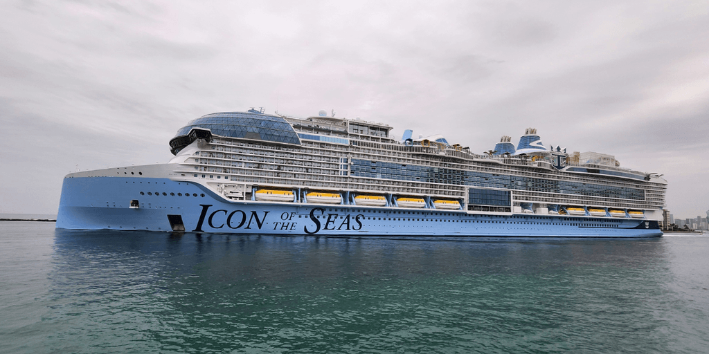 A cruise ship moored at a dock, reflecting in the water under a bright blue sky.
