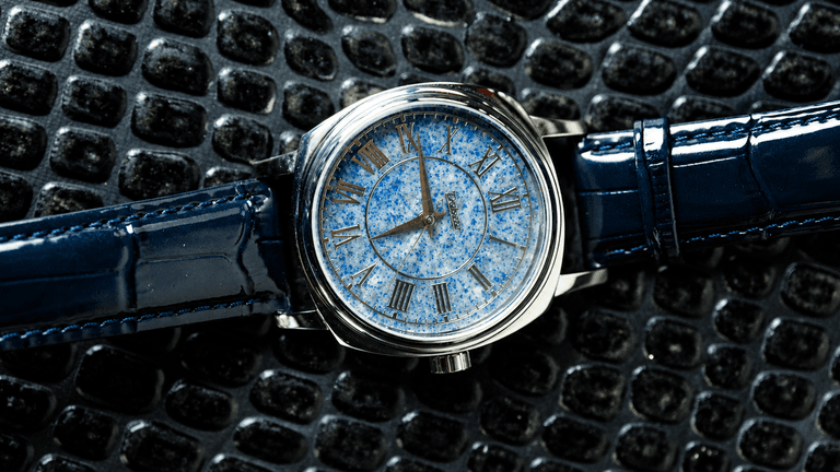 Elegant watch with a blue speckled dial and navy crocodile leather strap on textured surface