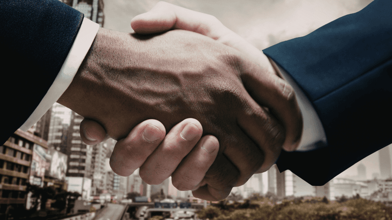 Two hands shake in a business setting with a cityscape in the background