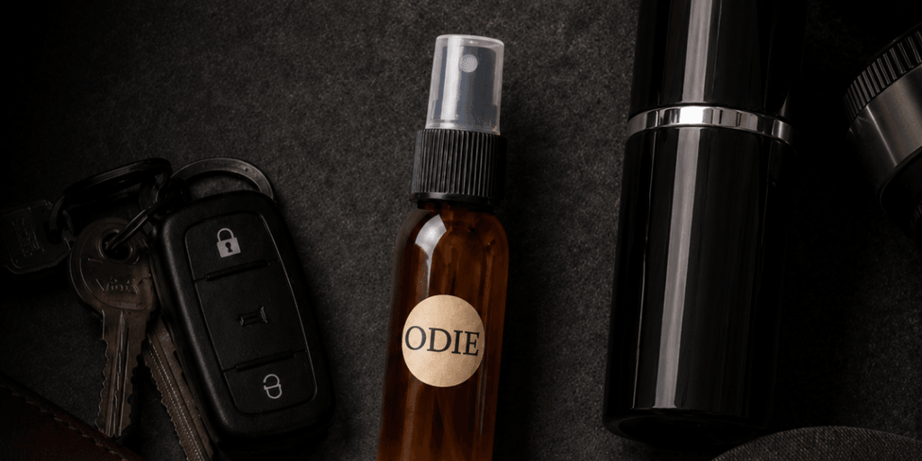 Flat lay of a brown spray bottle labeled "ODIE," car keys, and a black container