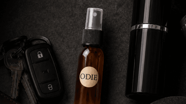 Flat lay of a brown spray bottle labeled "ODIE," car keys, and a black container