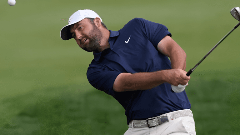 Golfer in a blue shirt swings to hit a golf ball on the course