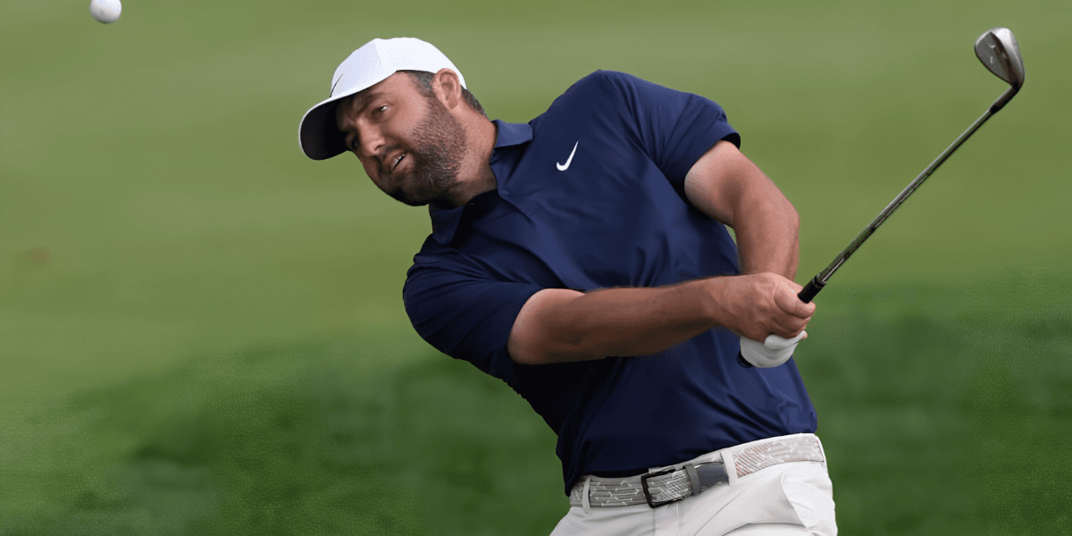 Golfer in a blue shirt swings to hit a golf ball on the course