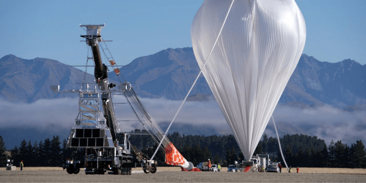 A large balloon being prepared for launch alongside a scientific equipment platform in a mountainous area