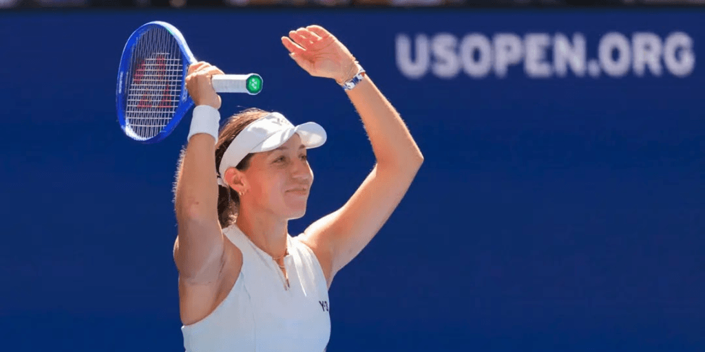 Smiling tennis player raises her arms in celebration on the court.