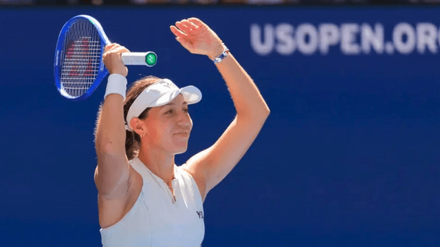 Smiling tennis player raises her arms in celebration on the court.