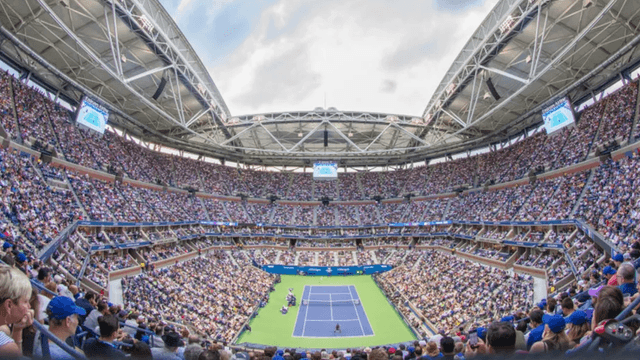 Packed stadium during a tennis match with a large audience and bright sky