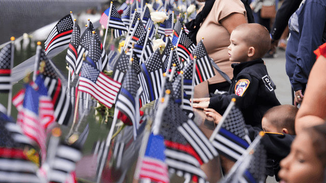 Children and adults observe flags and flowers in a memorial setting.
