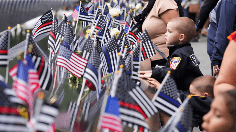 Children and adults observe flags and flowers in a memorial setting.