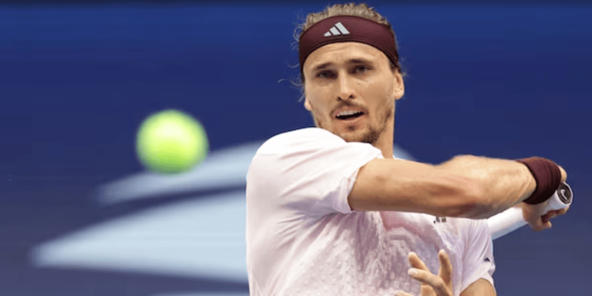 A male tennis player with long hair swings his racket at a ball.