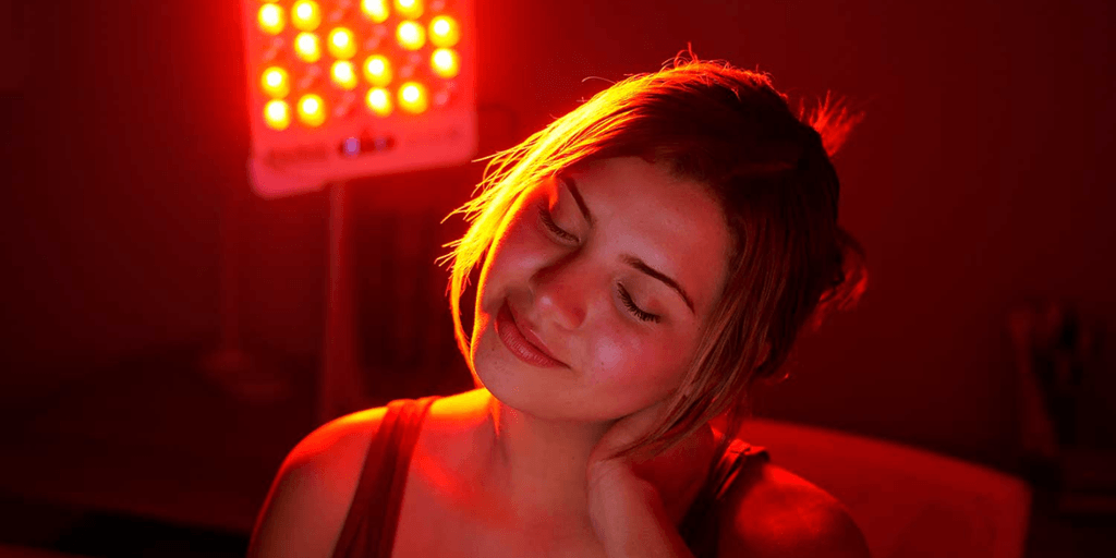 Woman enjoying red light therapy, relaxing with a gentle smile in dim lighting