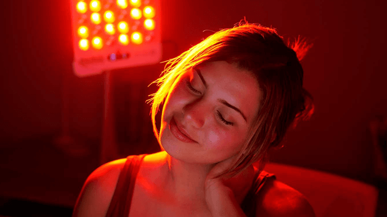Woman enjoying red light therapy, relaxing with a gentle smile in dim lighting