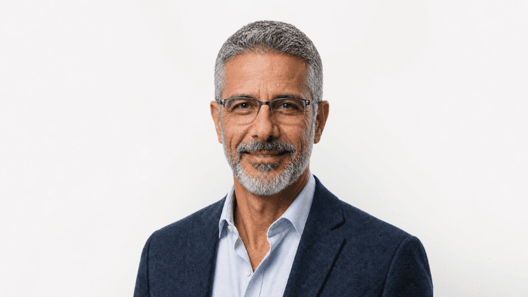 Smiling man with gray hair and glasses wearing a blue blazer over a white shirt