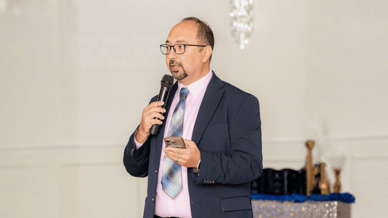 A man in a suit speaking into a microphone at an event