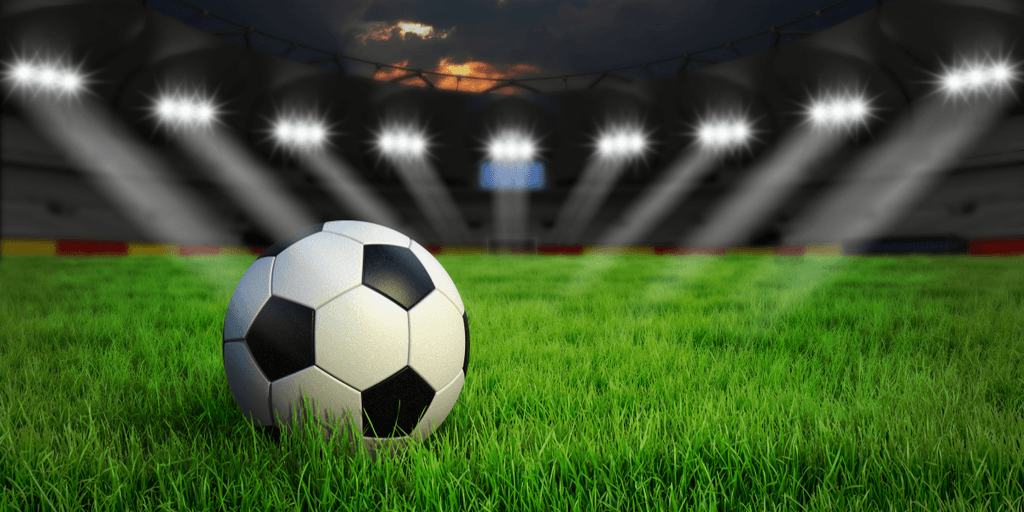 A soccer ball on a grassy field with stadium lights shining in the background