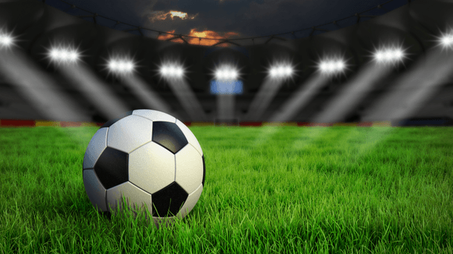 A soccer ball on a grassy field with stadium lights shining in the background
