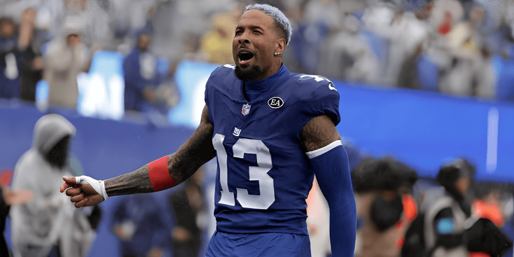 Football player in a blue jersey celebrates on the field with fans in the background