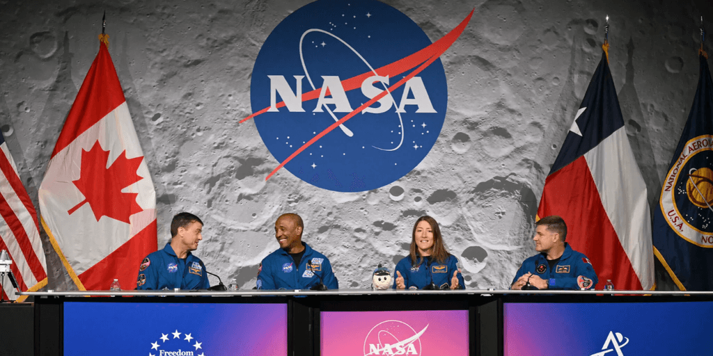 Astronauts at a NASA press conference with flags in the background