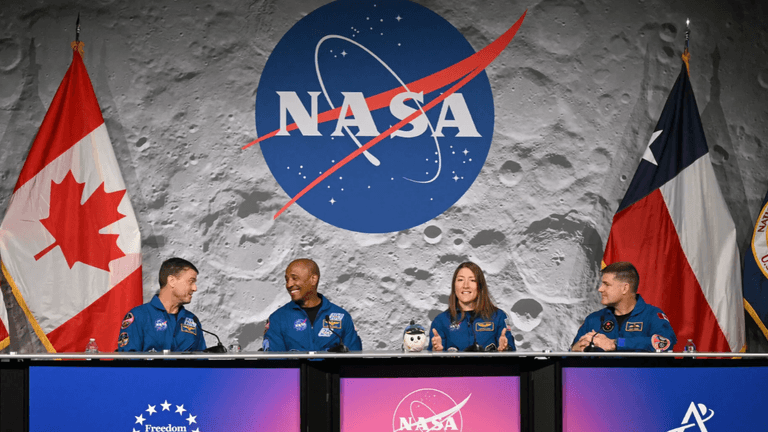 Astronauts at a NASA press conference with flags in the background