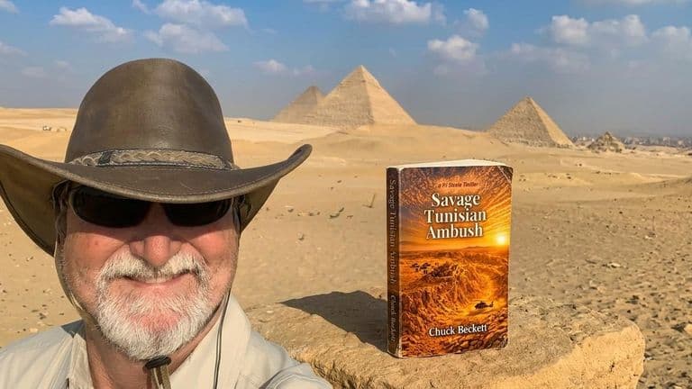 Man with a hat poses near pyramids, showcasing a book titled "Savage Tunisian Ambush"