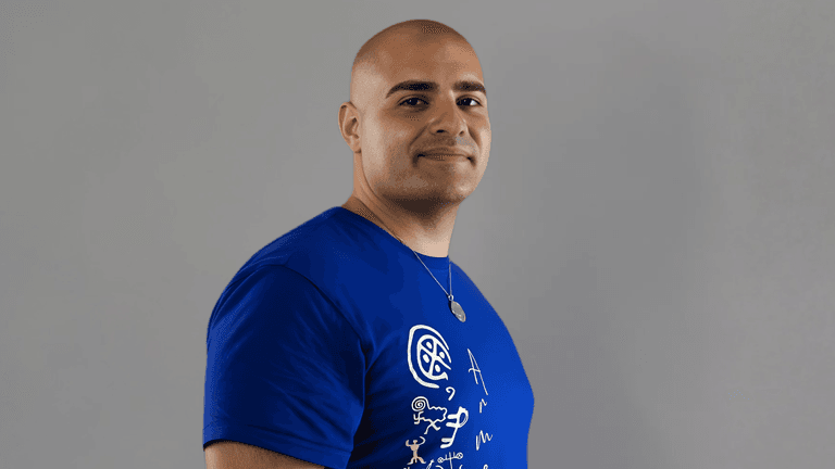 "Arthur Palyan, transformational life coach, smiling confidently in a blue t-shirt featuring the Seven Levels of Self framework design. Arthur’s teachings focus on helping individuals break free from survival mode and embrace conscious living."