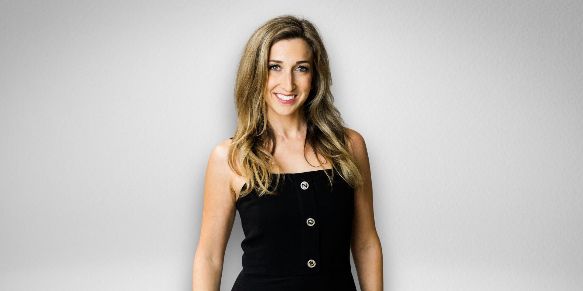 Professional headshot of Dara Rae Rahill smiling in a black dress against a gray background.