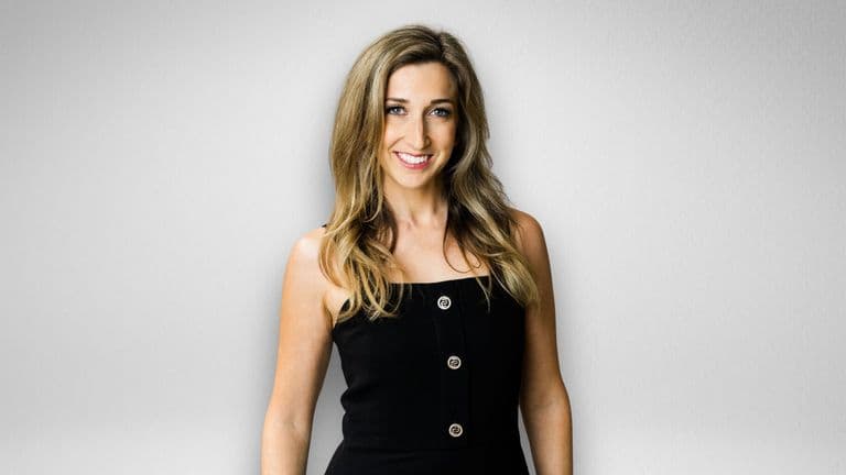Professional headshot of Dara Rae Rahill smiling in a black dress against a gray background.