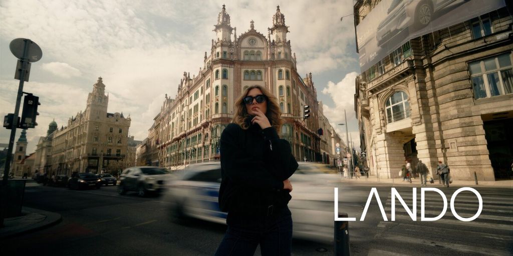 Person in sunglasses stands confidently on a busy city street, with ornate historic building in the background. Motion blur from passing cars adds dynamic energy.