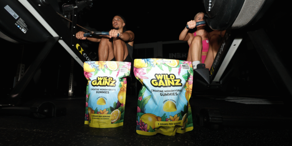 Wild Gainz creatine gummies displayed in a gym setting with athletes using rowing machines.