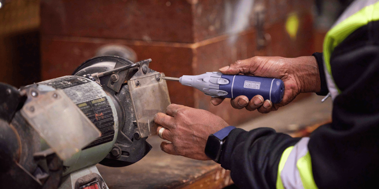 An African American technician uses a Kelvin Retractor Series screwdriver to secure a protective shield on a workbench grinder.
