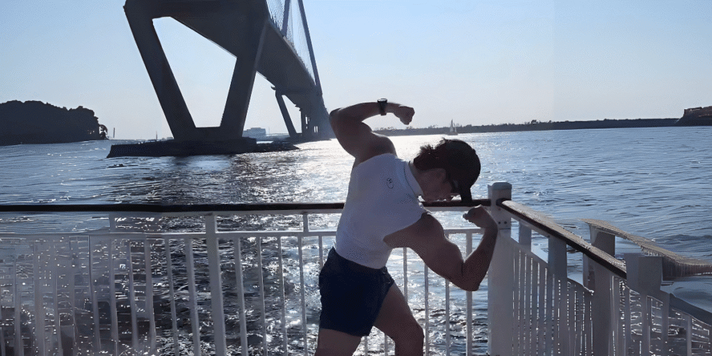 Brandon Stalter flexing by the water under a bridge, embodying strength, resilience, and transformation in his fitness journey.